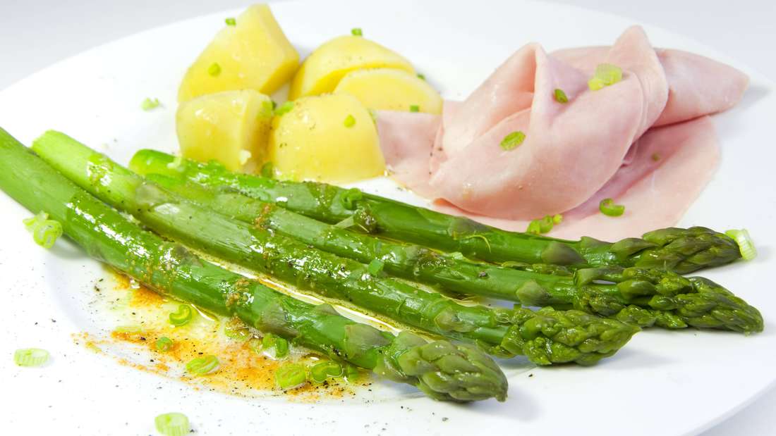 Green asparagus with butter sauce, cooked ham and potatoes on a plate.