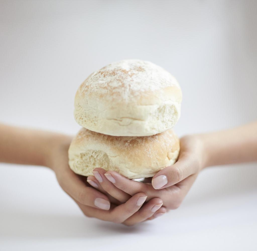 Close up of female hands holding two fresh soft white bread rolls with flour powdering and shallow focus.