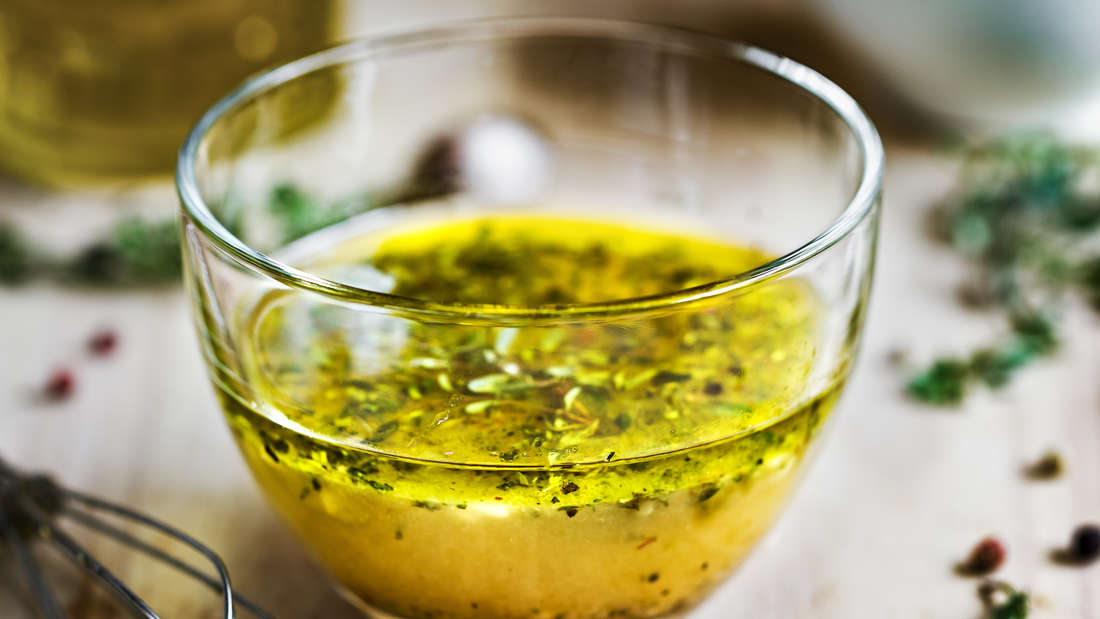 Classic vinaigrette with vinegar, oil, salt, pepper, thyme, fresh herbs in a bowl.  Next to it is a whisk 