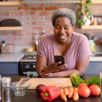 Woman stands in the kitchen and has a cell phone in her hand.  Counting calories can help you lose weight.